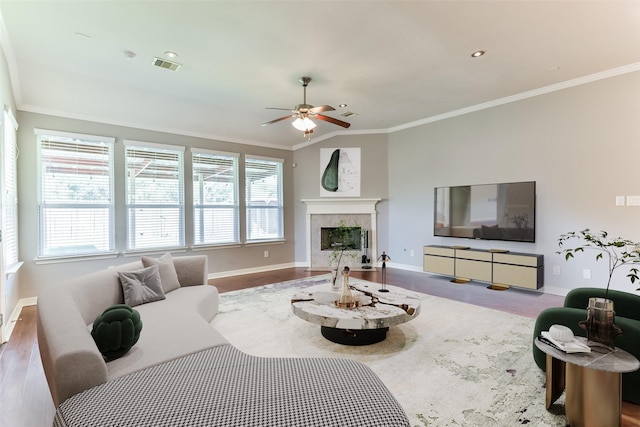 living room with ceiling fan, hardwood / wood-style flooring, a tile fireplace, and crown molding