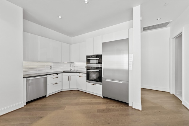 kitchen with sink, tasteful backsplash, light hardwood / wood-style floors, white cabinets, and appliances with stainless steel finishes