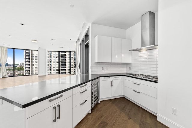 kitchen with white cabinetry, wall chimney exhaust hood, stainless steel gas cooktop, backsplash, and kitchen peninsula