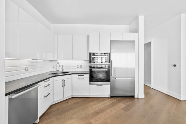 kitchen with sink, light wood-type flooring, tasteful backsplash, white cabinetry, and stainless steel appliances