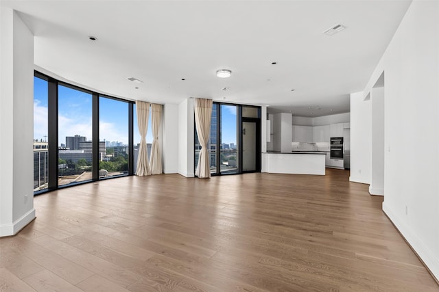 unfurnished living room with light wood-type flooring and a wall of windows