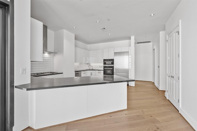 kitchen with kitchen peninsula, sink, white cabinets, and wall chimney range hood