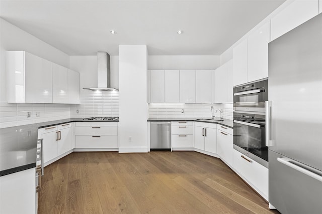 kitchen featuring light wood-type flooring, wall chimney exhaust hood, stainless steel appliances, sink, and white cabinetry