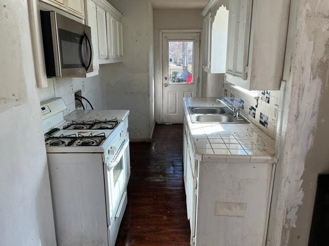 kitchen featuring tile countertops, white gas range, sink, and white cabinets