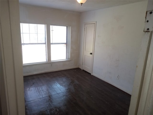 unfurnished room featuring baseboards and dark wood-type flooring