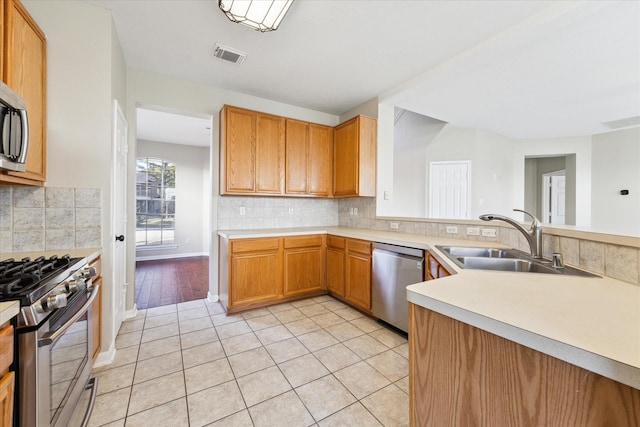 kitchen with backsplash, sink, appliances with stainless steel finishes, light tile patterned flooring, and kitchen peninsula