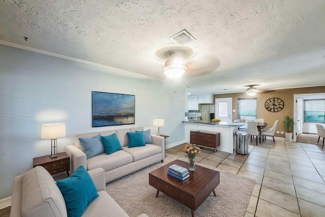 tiled living room featuring ceiling fan, ornamental molding, and a textured ceiling