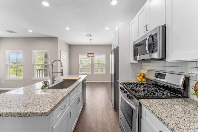 kitchen with white cabinets, sink, stainless steel appliances, and an island with sink