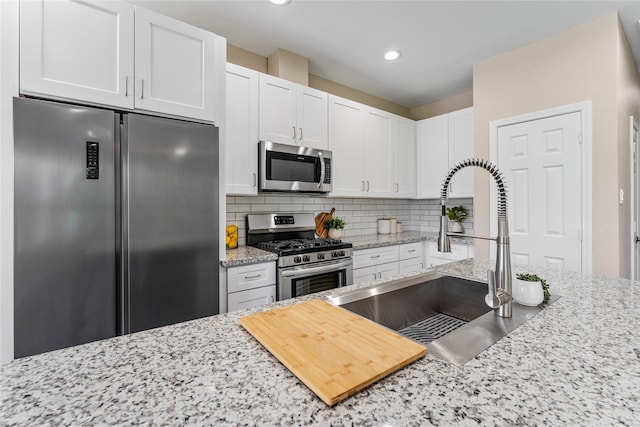 kitchen featuring light stone countertops, appliances with stainless steel finishes, backsplash, sink, and white cabinets