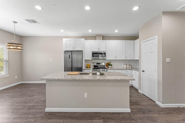 kitchen with white cabinets, light stone countertops, stainless steel appliances, and a kitchen island with sink