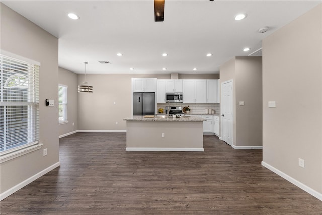 kitchen featuring a kitchen island with sink, decorative backsplash, appliances with stainless steel finishes, decorative light fixtures, and white cabinetry