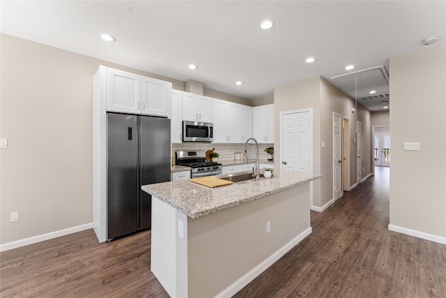 kitchen with a center island with sink, white cabinets, sink, appliances with stainless steel finishes, and light stone counters