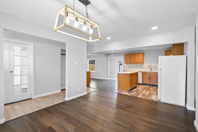 kitchen featuring pendant lighting, white appliances, sink, tasteful backsplash, and kitchen peninsula