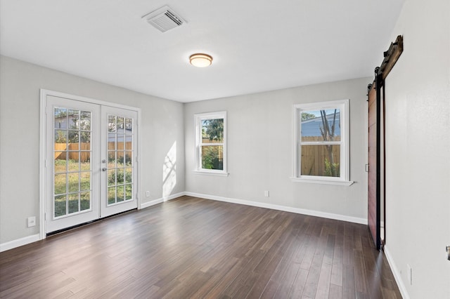 empty room featuring plenty of natural light, a barn door, dark hardwood / wood-style floors, and french doors