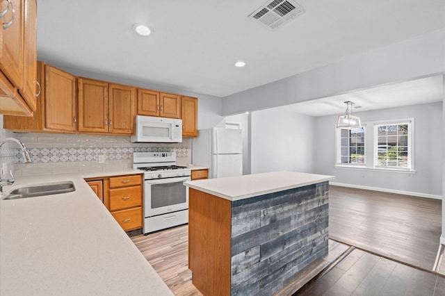 kitchen with sink, a center island, hanging light fixtures, light hardwood / wood-style floors, and white appliances