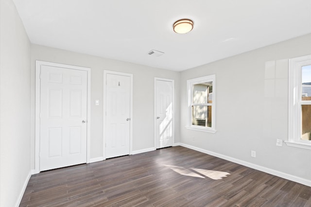 unfurnished bedroom with multiple windows, dark hardwood / wood-style flooring, and two closets