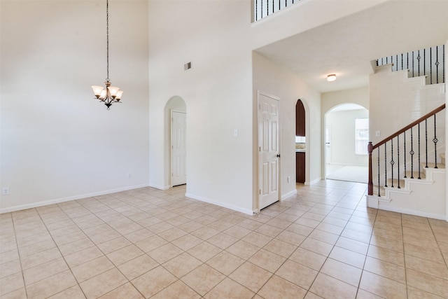 unfurnished room featuring a towering ceiling, an inviting chandelier, and light tile patterned flooring