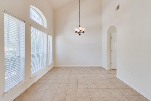 empty room with a towering ceiling, light tile patterned flooring, and an inviting chandelier