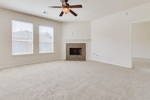 unfurnished living room with a tile fireplace, ceiling fan, and light colored carpet