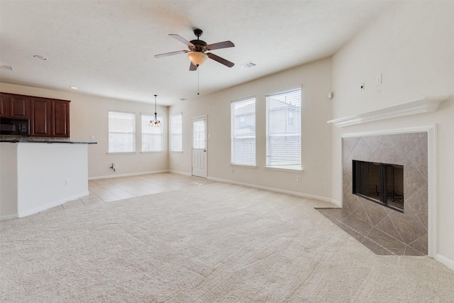 unfurnished living room with a fireplace, ceiling fan with notable chandelier, and light colored carpet