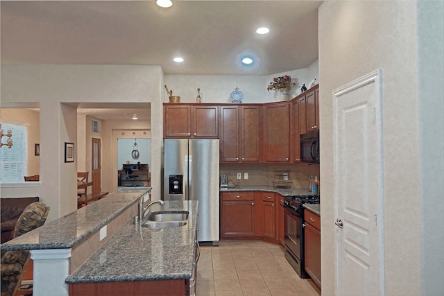 kitchen featuring sink, dark stone countertops, an island with sink, light tile patterned flooring, and black appliances