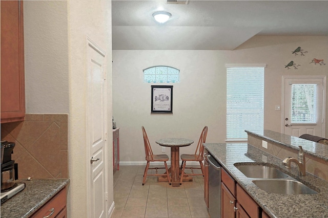 kitchen with dishwasher, light tile patterned flooring, dark stone countertops, and sink