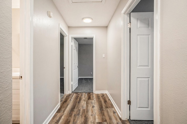 hallway featuring attic access, dark wood finished floors, and baseboards