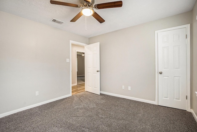 carpeted empty room with a textured ceiling, a ceiling fan, visible vents, and baseboards