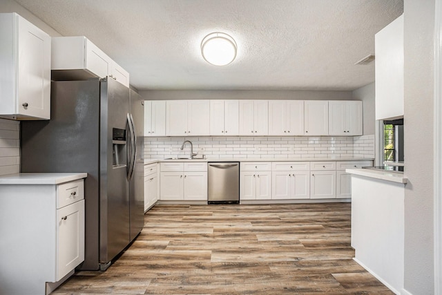 kitchen featuring stainless steel appliances, a sink, white cabinetry, light wood-style floors, and decorative backsplash