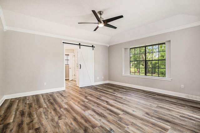 empty room with ornamental molding, a barn door, wood finished floors, and baseboards