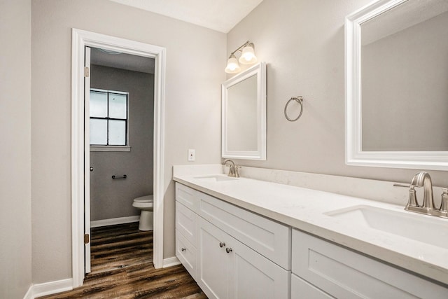 bathroom featuring double vanity, wood finished floors, a sink, and toilet