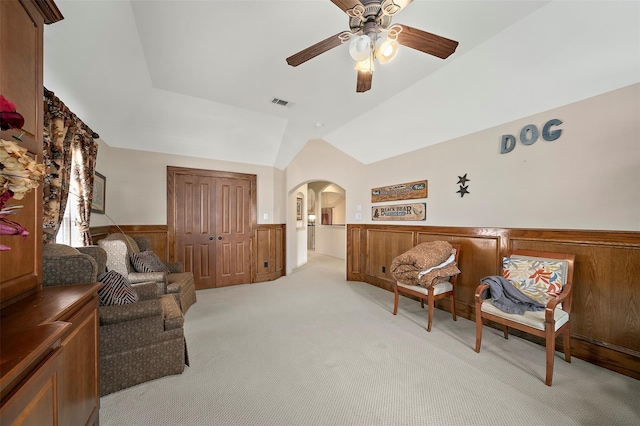 living area with light colored carpet, ceiling fan, lofted ceiling, and wood walls