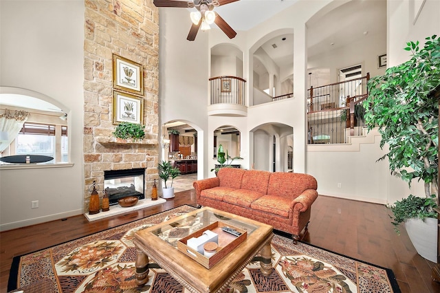 living room with a high ceiling, a stone fireplace, ceiling fan, and wood-type flooring