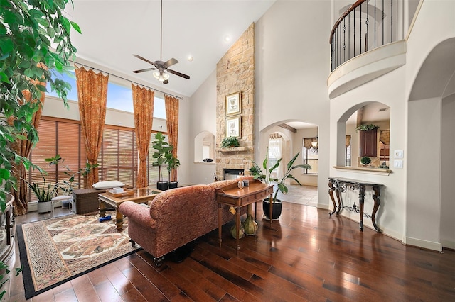 living room featuring dark hardwood / wood-style floors, ceiling fan, a stone fireplace, and a towering ceiling