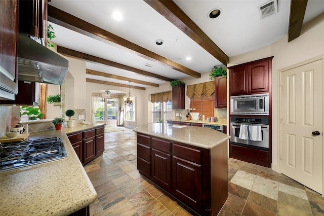 kitchen with light stone countertops, a center island, stainless steel appliances, beamed ceiling, and range hood