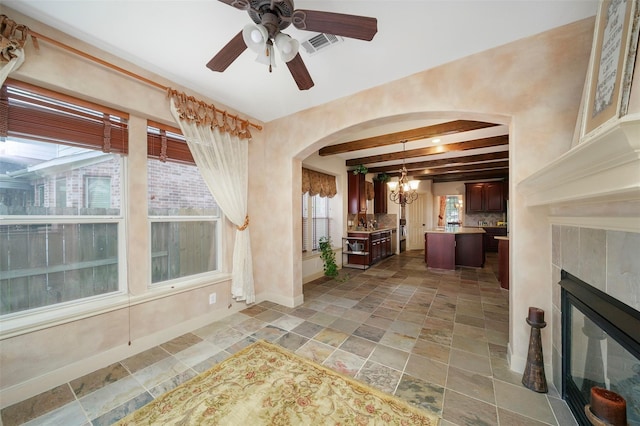 interior space with beamed ceiling, ceiling fan with notable chandelier, and a tiled fireplace