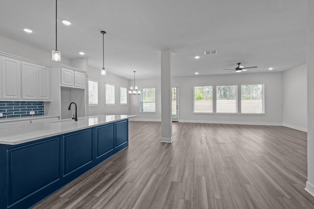 kitchen with white cabinets, ceiling fan with notable chandelier, light hardwood / wood-style flooring, decorative backsplash, and a healthy amount of sunlight