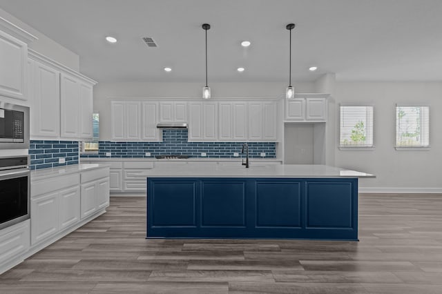 kitchen featuring decorative backsplash, appliances with stainless steel finishes, a center island with sink, white cabinetry, and hanging light fixtures