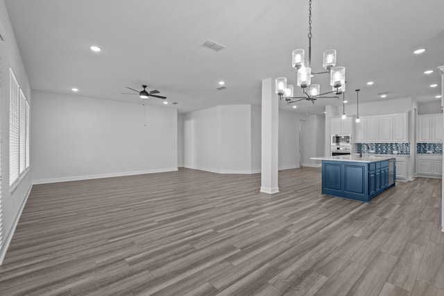 kitchen featuring backsplash, stainless steel appliances, blue cabinetry, a center island with sink, and white cabinets