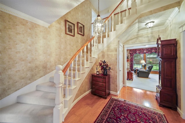 staircase featuring an inviting chandelier, a towering ceiling, crown molding, and hardwood / wood-style floors