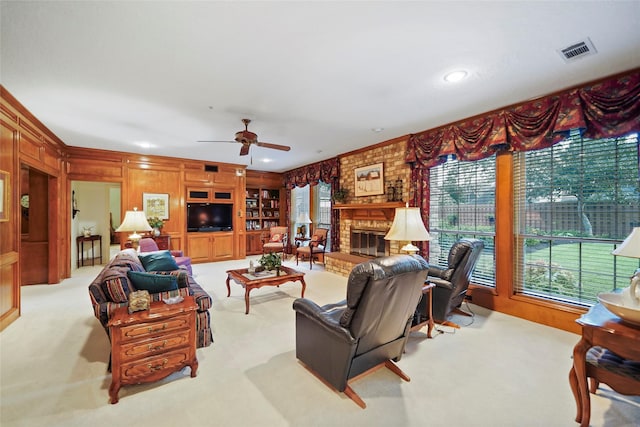 carpeted living room featuring a brick fireplace, built in shelves, a wealth of natural light, and ceiling fan