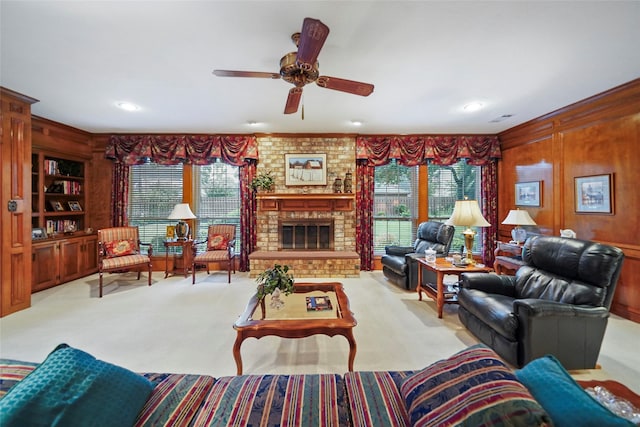 carpeted living room featuring a brick fireplace, built in shelves, wood walls, and ceiling fan