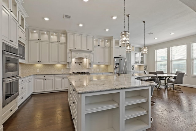 kitchen with white cabinetry, stainless steel appliances, light stone counters, pendant lighting, and a spacious island