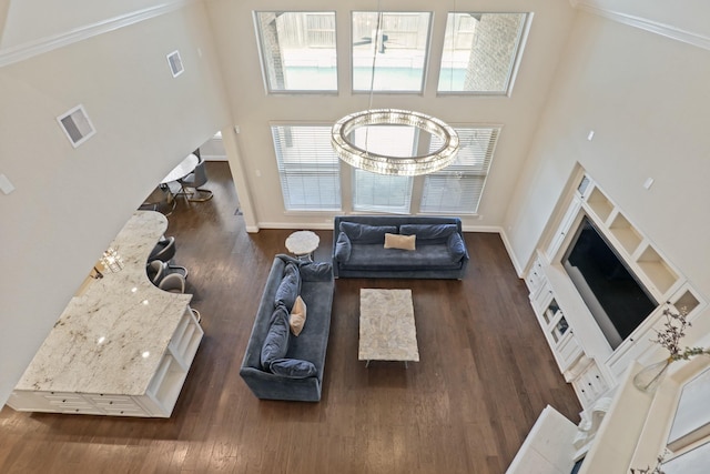 living room with dark hardwood / wood-style flooring, a towering ceiling, an inviting chandelier, and ornamental molding