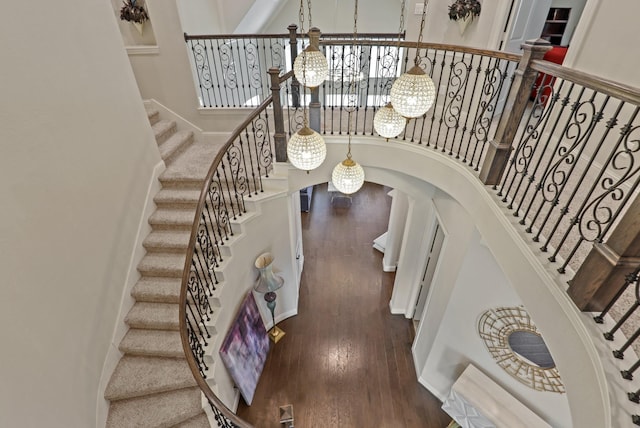 stairway with a notable chandelier, wood-type flooring, and a towering ceiling