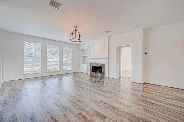 unfurnished living room featuring built in shelves, a premium fireplace, light hardwood / wood-style flooring, and an inviting chandelier