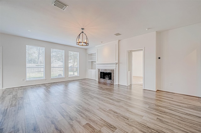 unfurnished living room featuring visible vents, light wood-type flooring, an inviting chandelier, and built in features