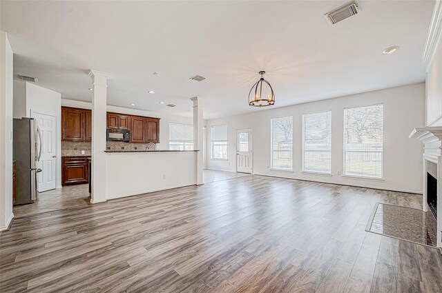 unfurnished living room with decorative columns, light hardwood / wood-style floors, and a notable chandelier