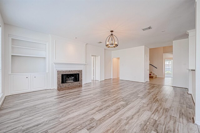 unfurnished living room featuring light wood-type flooring, visible vents, a tiled fireplace, stairway, and a chandelier