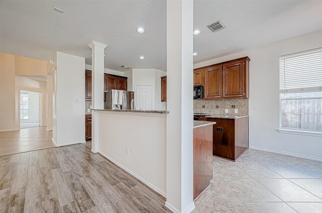 kitchen with visible vents, decorative columns, stainless steel fridge, black microwave, and decorative backsplash